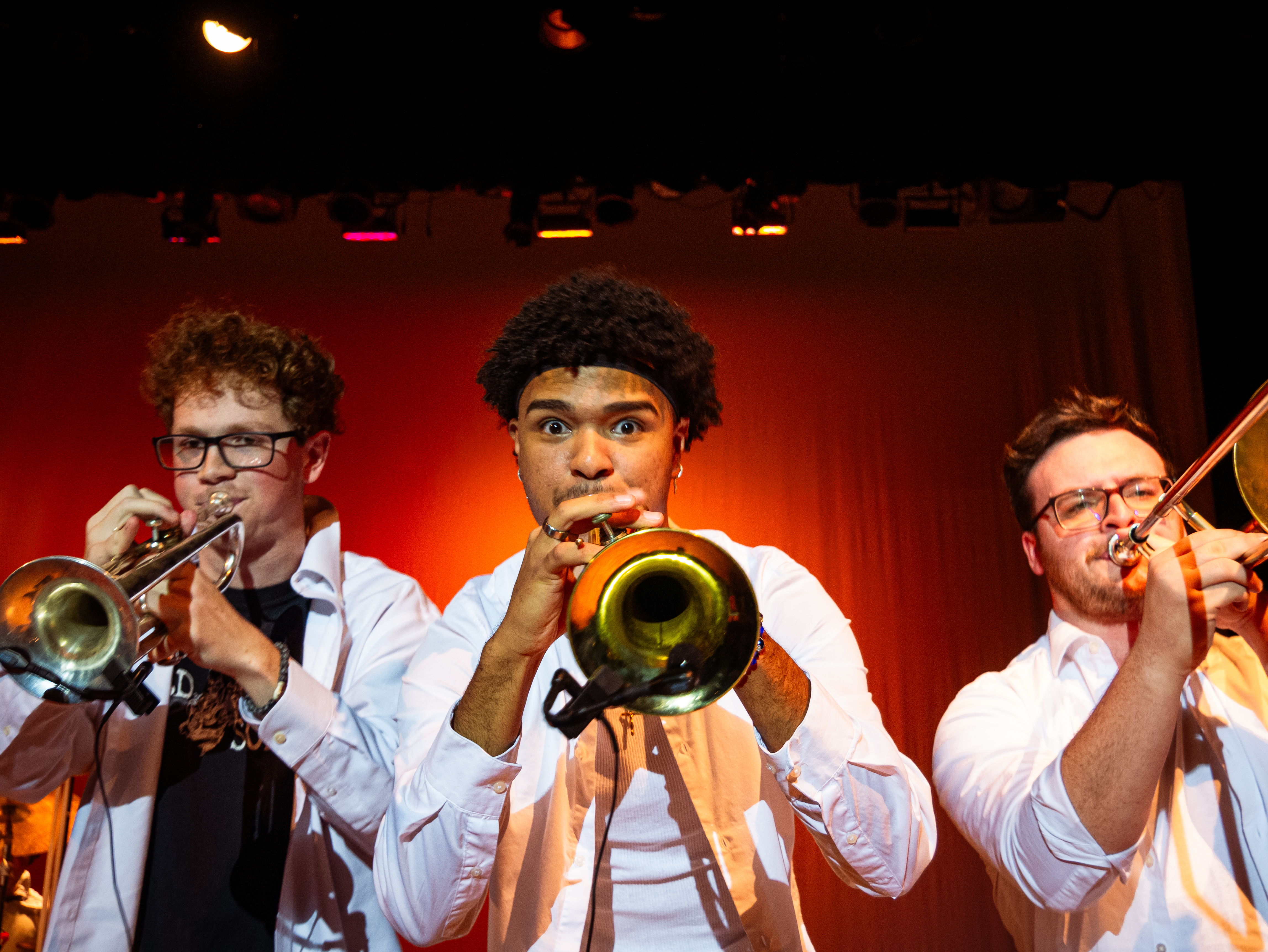 Three students playing brass instruments on stage close to photographer. 
