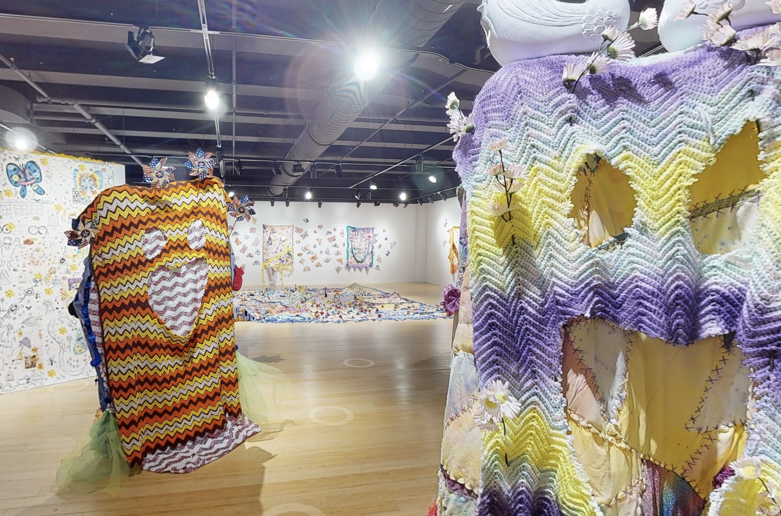 Wide shot of woven cloth art installations that have faces cut into them on the gallery floor 