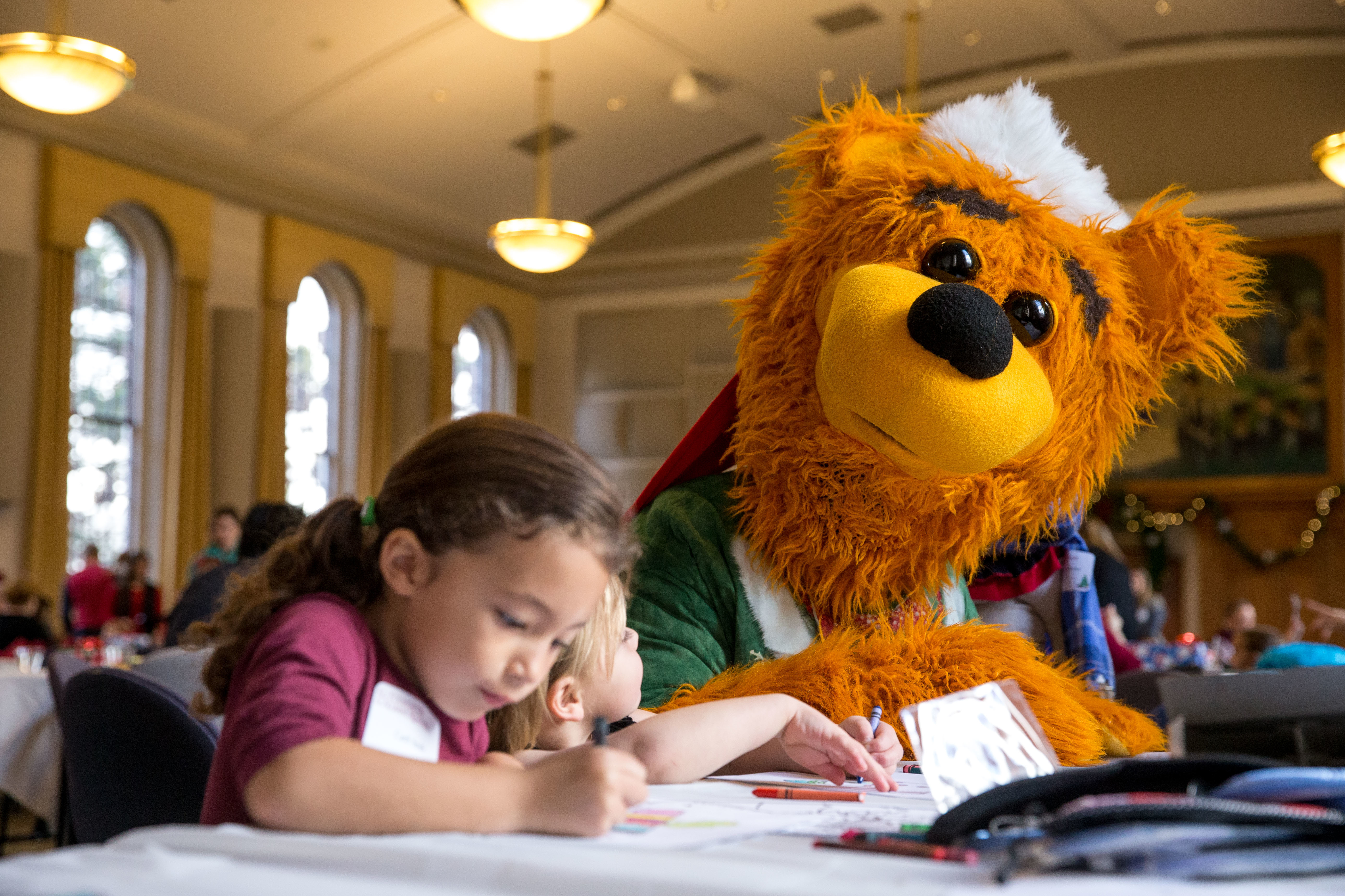 Avalanche sitting next to a child. Avalanche is looking at the child while the child appears to be reading and writing on paper.