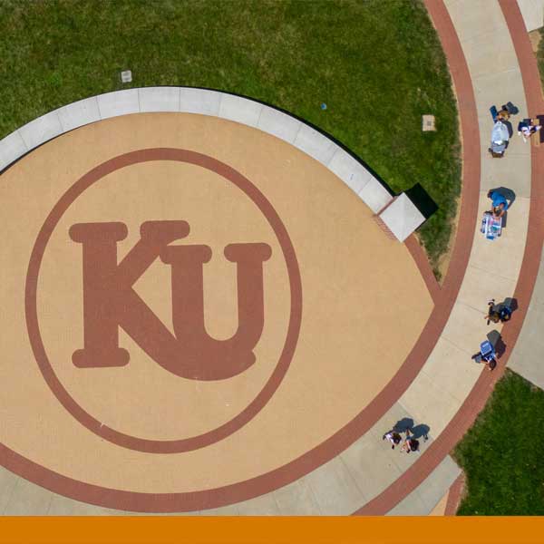 a birds eye view of the Kutztown University logo on a concrete patio of the residence hall with a few students and families moving their belongings into the residence halls.