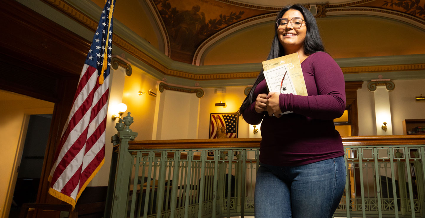 image of a female holding a binder standing in a large room next to an american flag