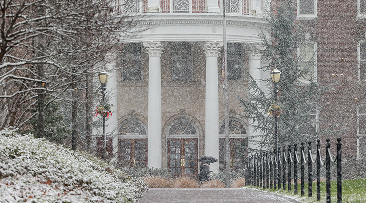 A snowy scene showing the front of old main as pedestrians walk by.