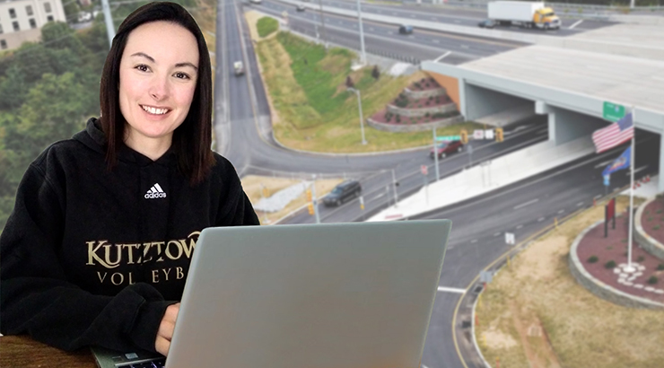 Female student smiling and holding a laptop in front of a green screen which displays two roads merging under a bridge 