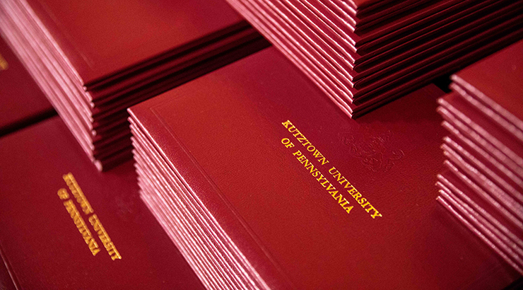 Closeup on a stack of Kutztown University Degree booklet covers, which say "Kutztown University of Pennsylvania" 