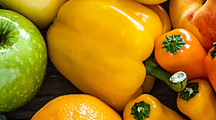 Closeup on produce, including yellow and orange bell peppers, green apples, and oranges 