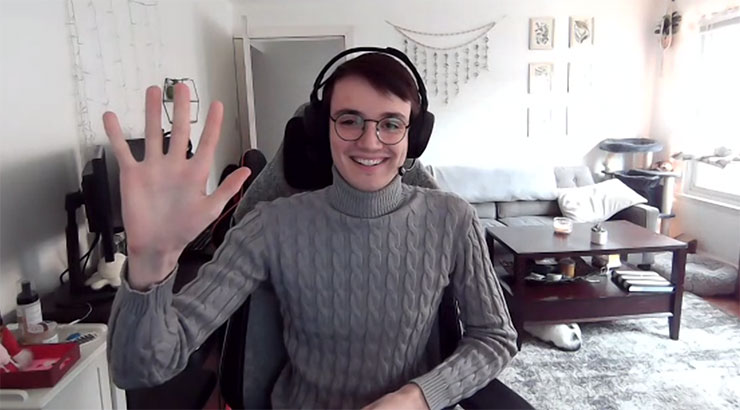 Connor Ellis, wearing a headset, smiling and waving at the screen over a virtual conference 