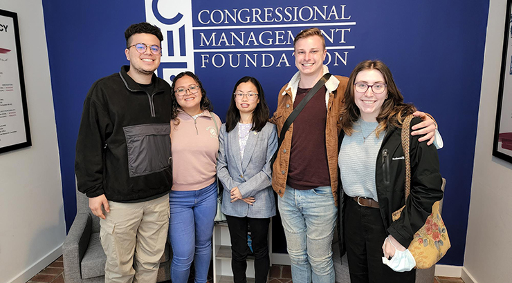 Students and faculty smiling in front of a wall with the congressional management foundation logo 
