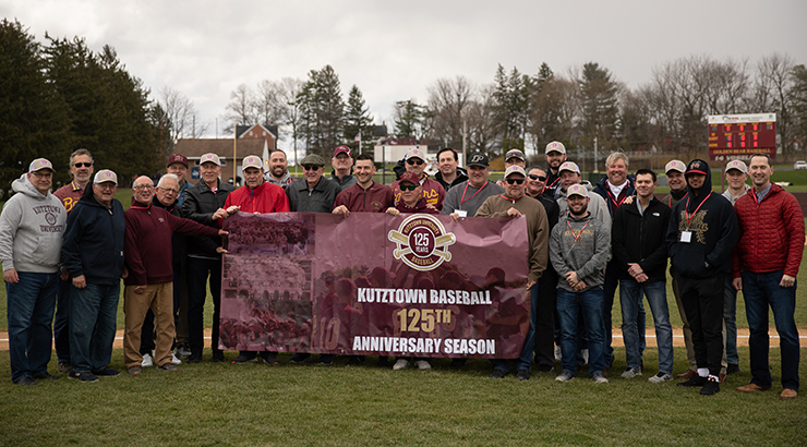 KU baseball team smiling and holding up a banner that says "Kutztown Baseball 125th Anniversary Season" 