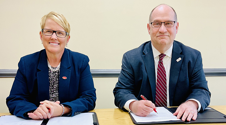Dr. Susan Looney (left) Dr. Hawkinson (right) smiling behind a desk and holding a pen up over a stack of papers 