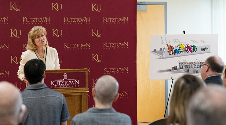 Judy Schwank smiling behind a podium with the Kutztown University logo and addressing a crowd 