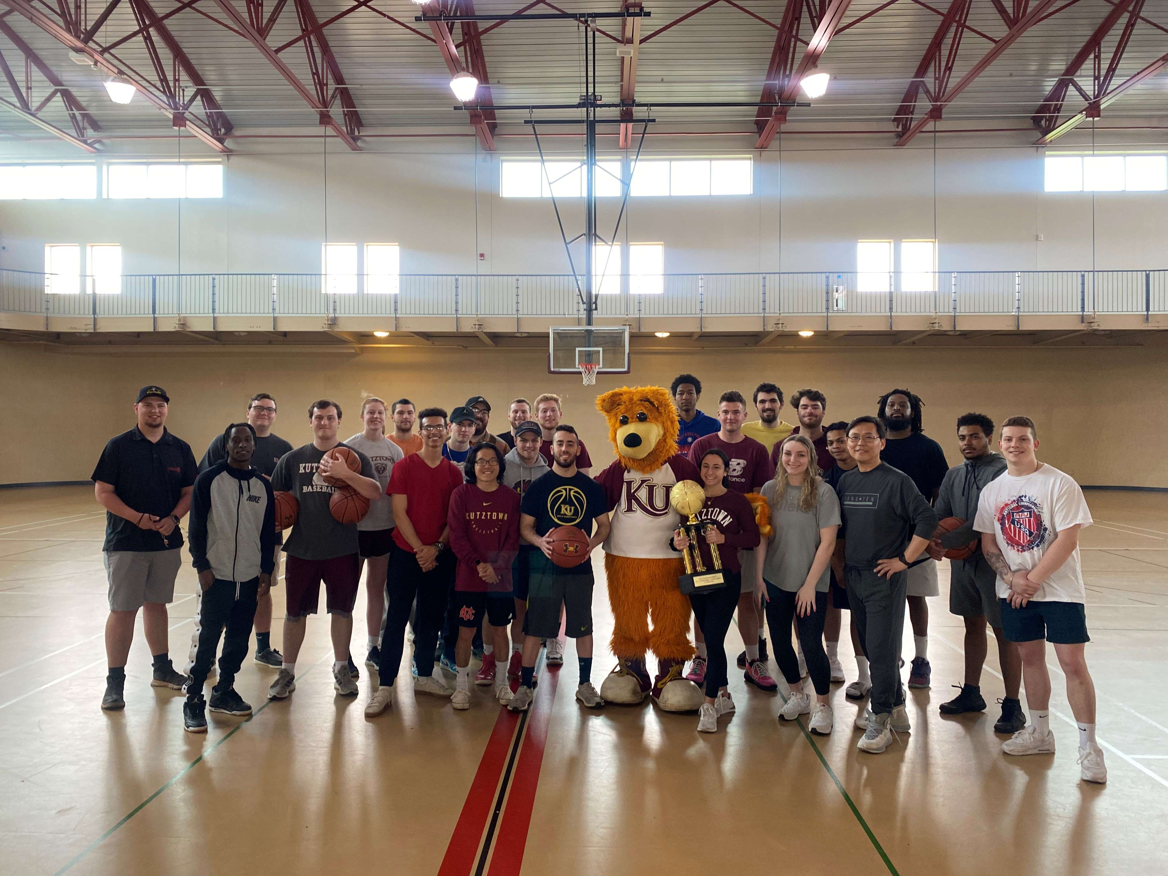 KU basketball team players, coaches, and Avalanche smiling in a group in the gymnasium 