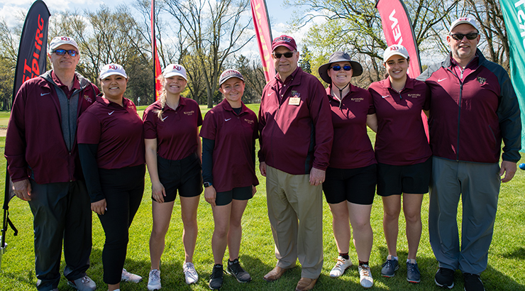 President Hawkinson in a group with the women's golf team on the field, all of them wearing KU Nike branded uniforms
