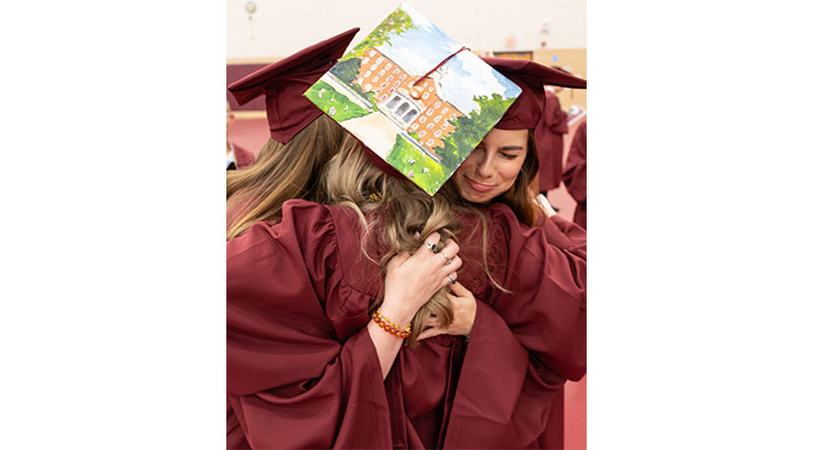 Old Main painted on a cap of graduates hugging