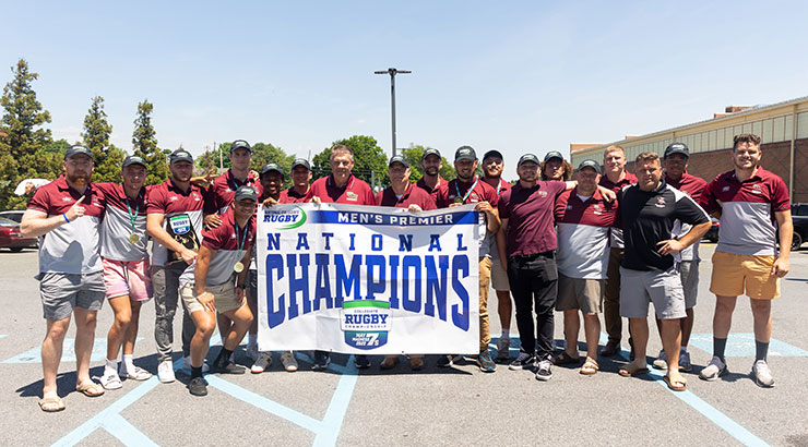 Rugby team poses with national championship banner upon return to KU.