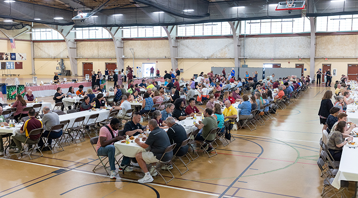 Faculty and Staff seated at several long tables in the gymnasium, eating lunch