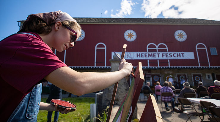 Photo of a woman painting at the festival with the barn in the background