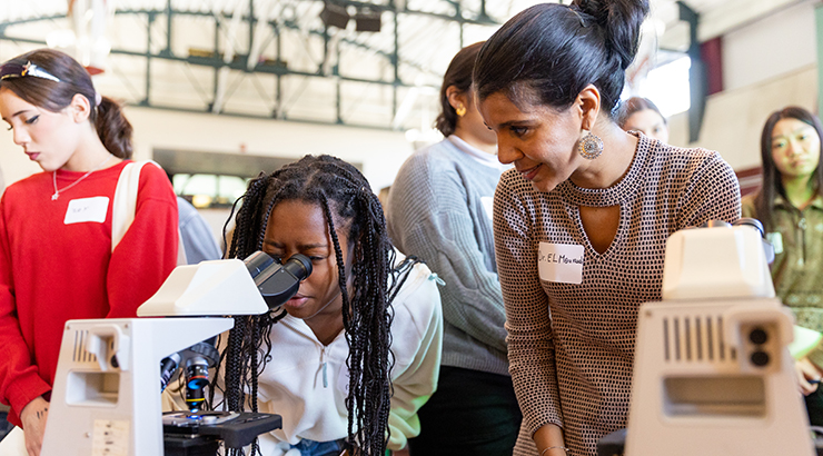 Female teacher with female student looking through microscope