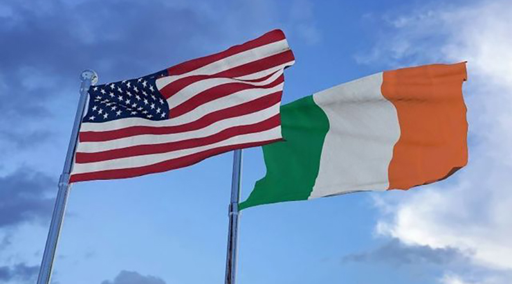 American flag and Irish flag flying on flagpoles next to each other, with the blue sky in the background 