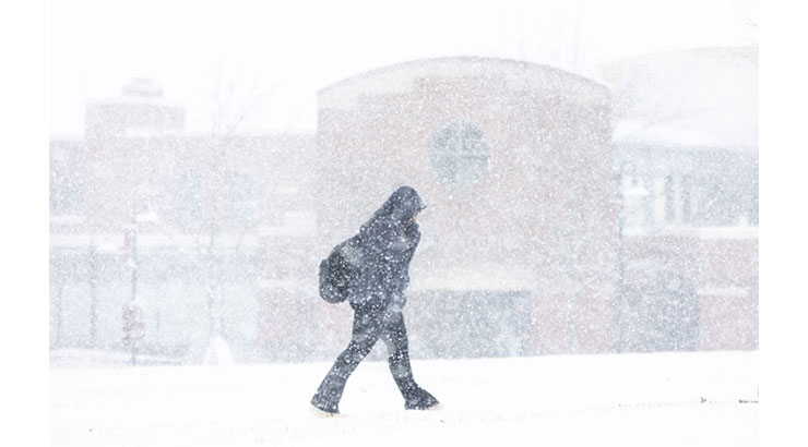 Photo of person dressed in dark clothing walking in a white wonderland on campus.