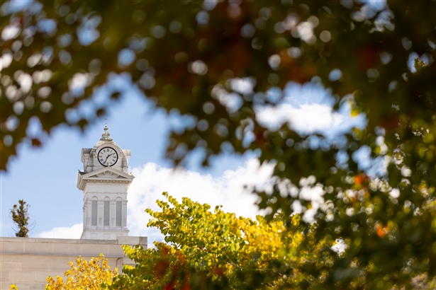 Photo of Old Main clock tower through fall trees.