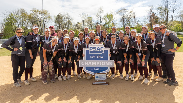 KU Softball team standing in a group on the softball field and holding a sign that reads "PSAC Softball Champions 2022" 