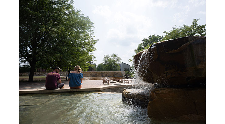 Two students sitting at the rock fountain at Alumni Plaza.