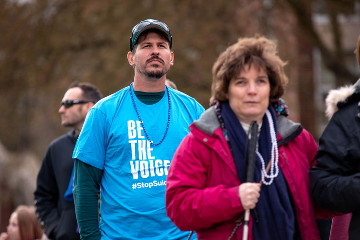 Participants in the walk, focusing on a man wearing a shirt that says "Be the voice; stop suicide."