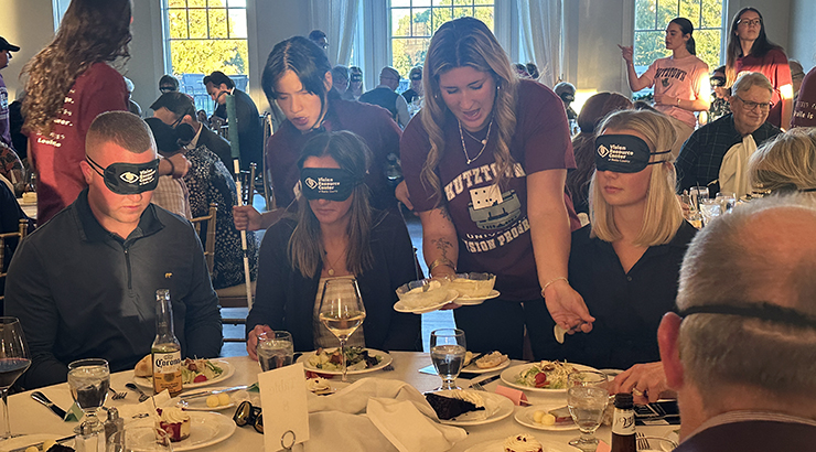 Students helping people eat at table with blindfolds on
