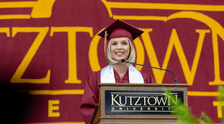 Morgan Harrar dressed in commencement regalia speaking at graduation.