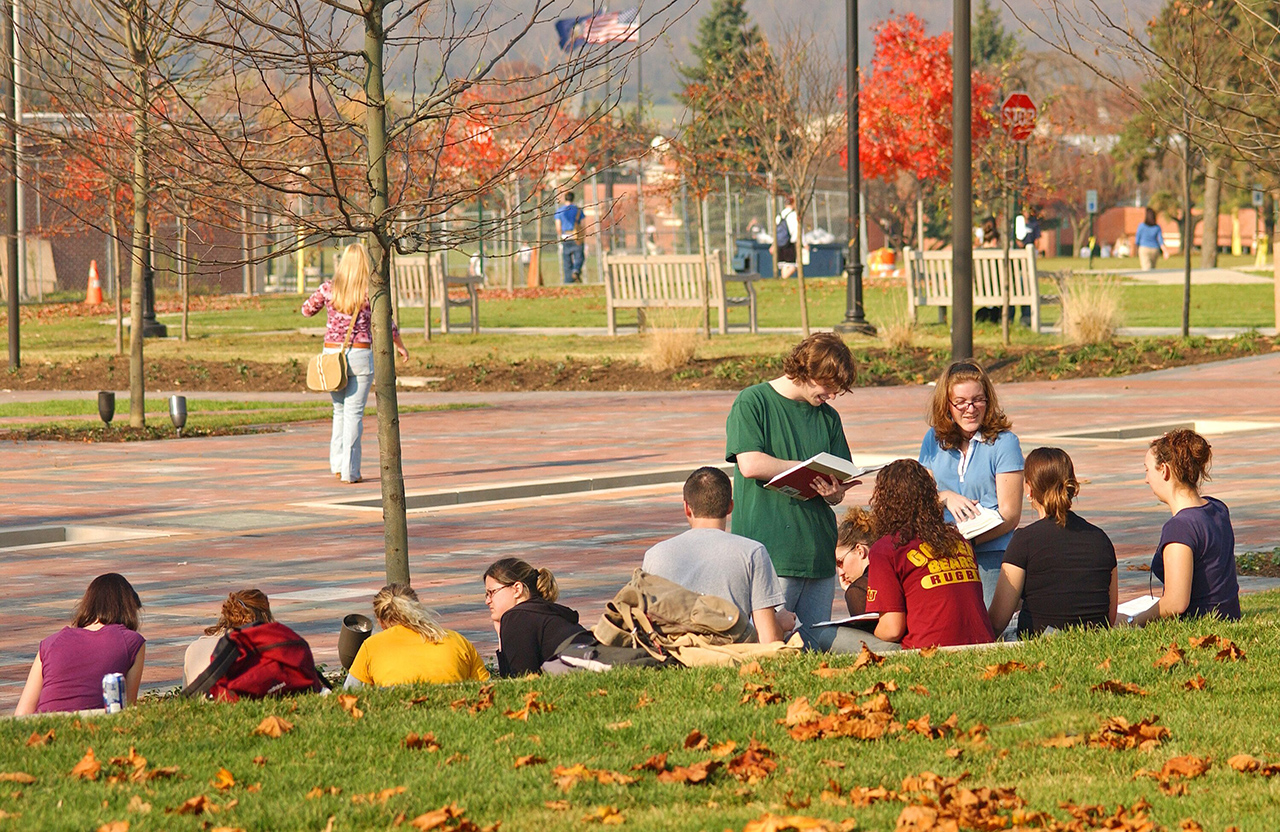 A group of students sitting on the benches and studying in the plaza during the fall, with more students walking around the courtyard in the background 