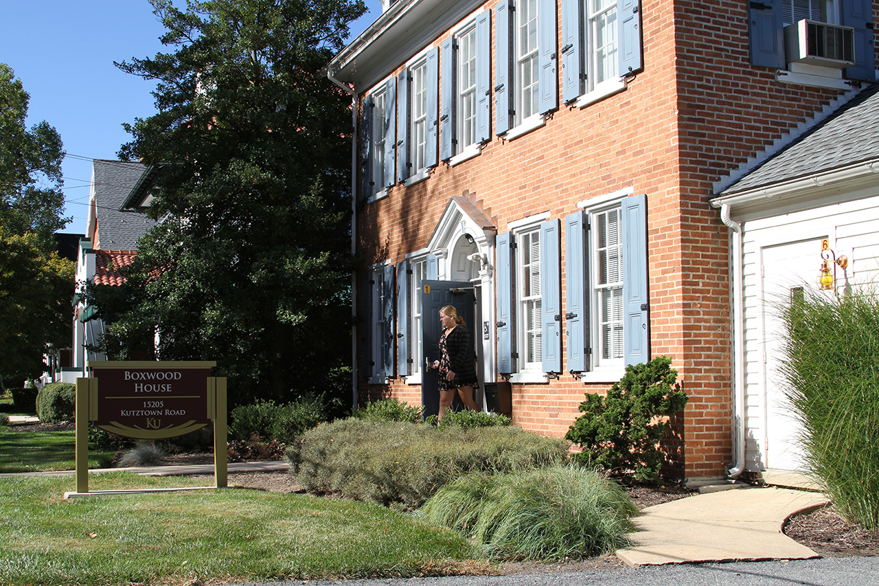Female student leaving the front entrance of Boxwood house with the building sign in the foreground 