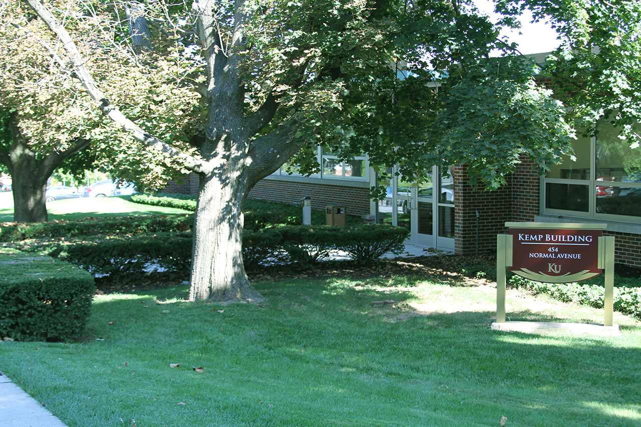 Front path and welcome sign to the Kemp Building, with large trees in the foreground 