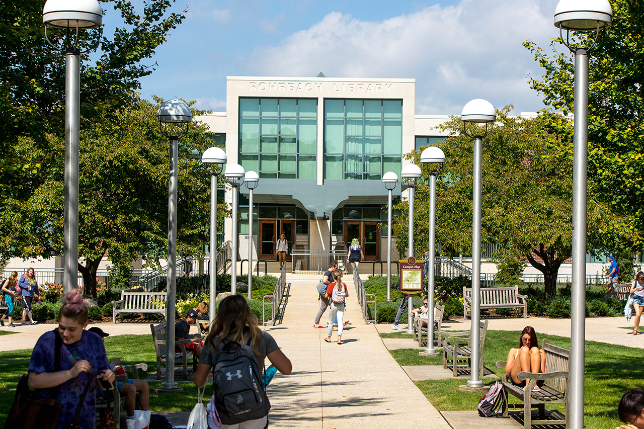 Entrance of Rohrbach Library with students walking around and studying in the foreground
