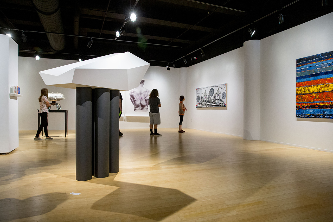 Four students walking around and looking at the paintings in the Miller gallery, with an abstract sculpture in the foreground