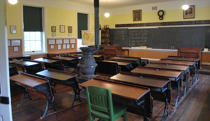 Old style classroom with rows of large wooden desks and an old furnace in the center