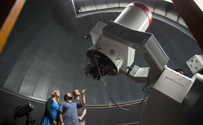 student and faculty staring up at a large (human-sized) telescope