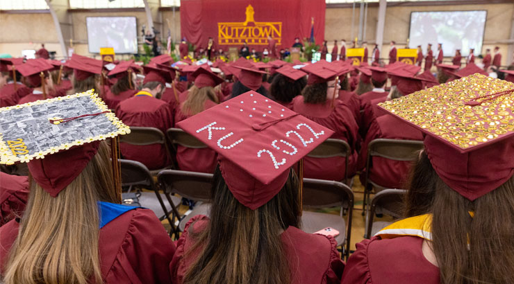Graduates in caps and gowns during commencement.  In the foreground are three students wearing decorated caps, the one in the middle reading "KU 22022"