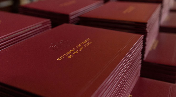 Stacks of maroon Diploma covers. On one in the foreground, the wording Kutztown University of Pennsylvania is visible.