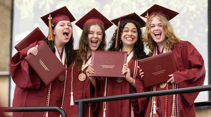 Group of female graduates in cap and gown regalia holding diplomas.