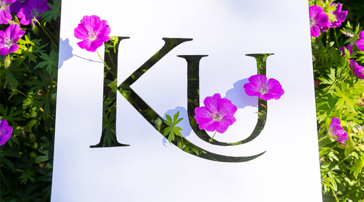 colorful flowers peak out around and through a cutout of the KU logo on a piece of paper. 