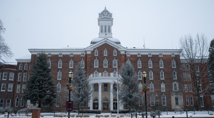 The front of Old Main, with snow on the ground below the entrance and iconic clock tower.