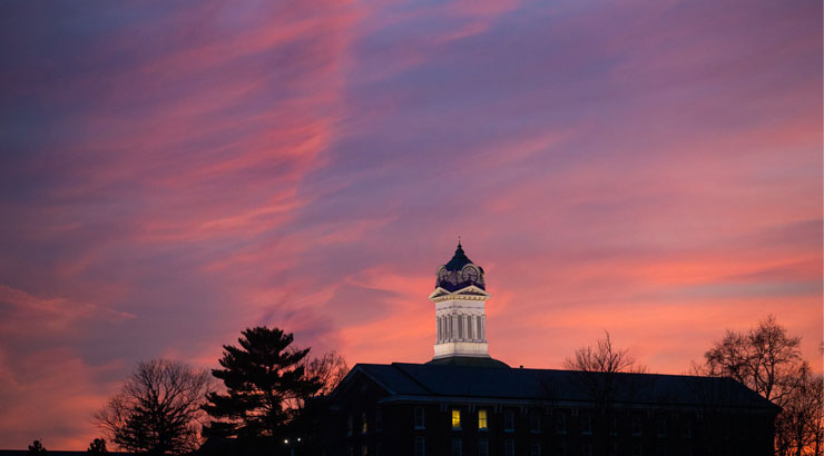 A view of Old Main, including the clock tower, wtih a colorful sunset backdrop.