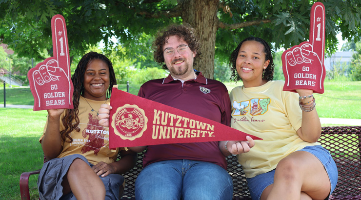 Three students wearing Kutztown University Maroon and Gold and school spirit gear.