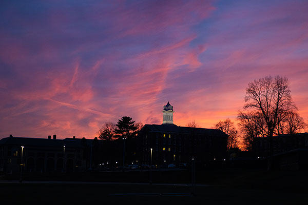 The silhouette of the old main building and clock tower against a vibrant blue red and yellow sunset sky