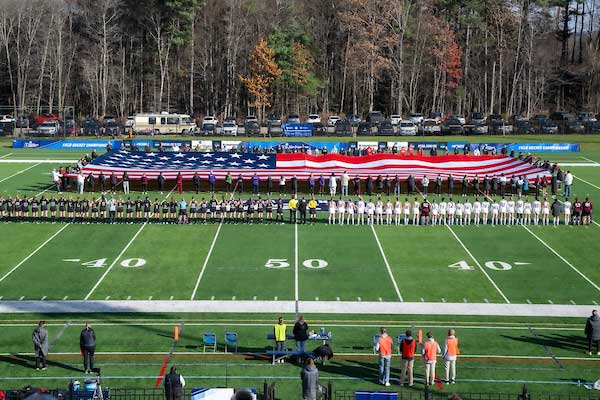 Pre-game national anthem, players and coaches on the field with large American Flag.