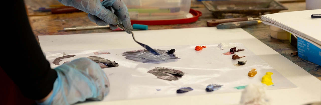 hands of an artist mixing paints with a tool to create new colors