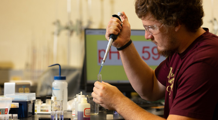 Male student wearing goggles while working in biochemistry degree lab space.