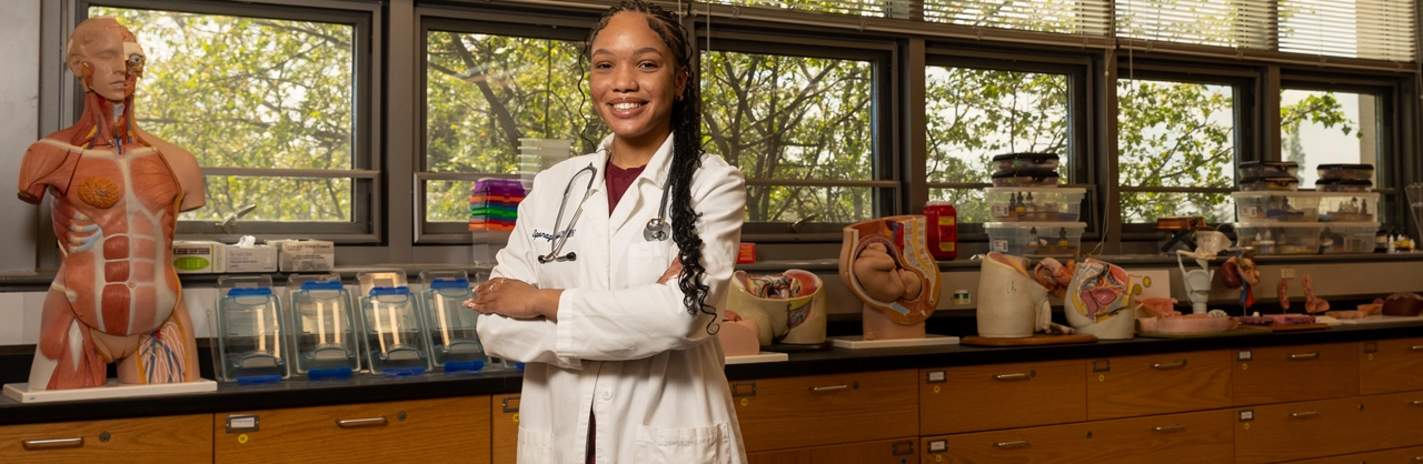 Female pre-med student stands with arms crossed in a science lab on Kutztown University's campus.