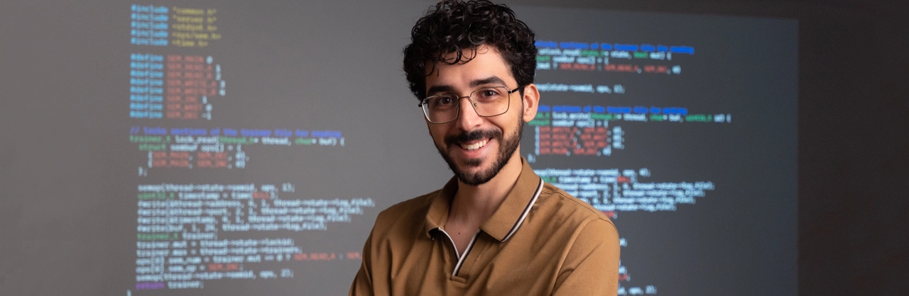 A male student standing in front of a screen with code on it