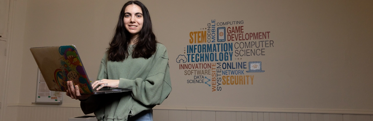 A female computer science student holding a laptop and typing